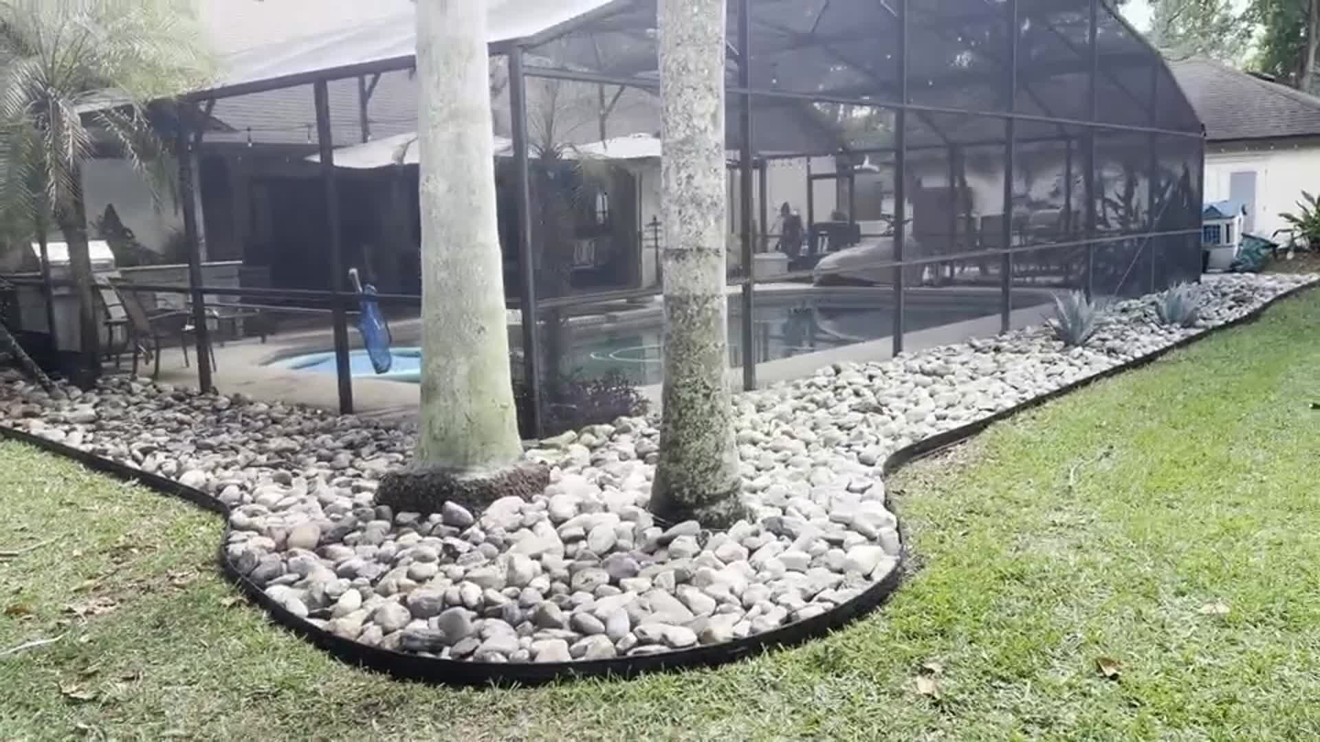 River rock border edging around palm trees beside a screened pool