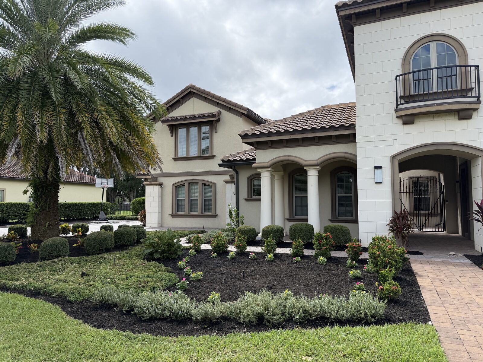 Fresh mulch bed and new plantings beside a paver walkway at a stucco home