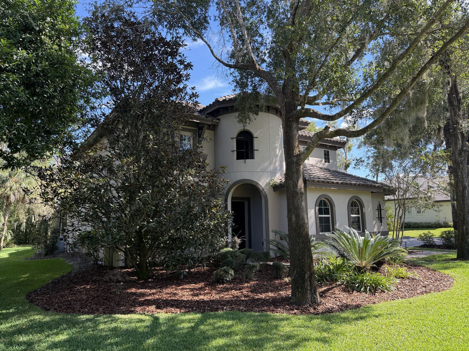 Curved mulch bed with shrubs in front of a home under large oak trees