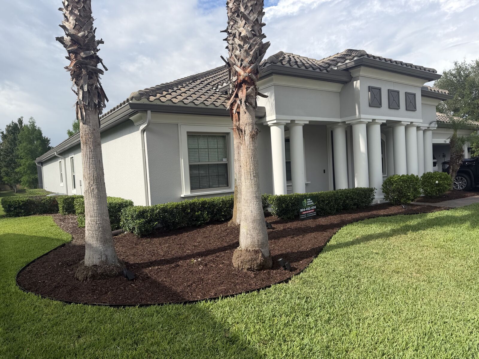 Metal edging border around a brown mulch bed with two palms in front of a home
